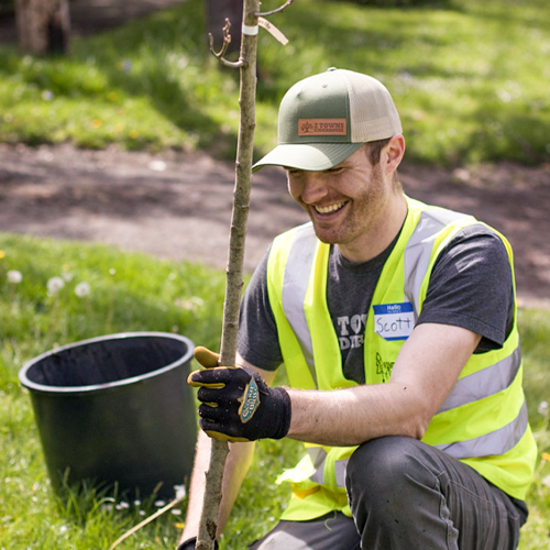 Nature Never Stops. 2 Towns employee smiles as he plants a tree.